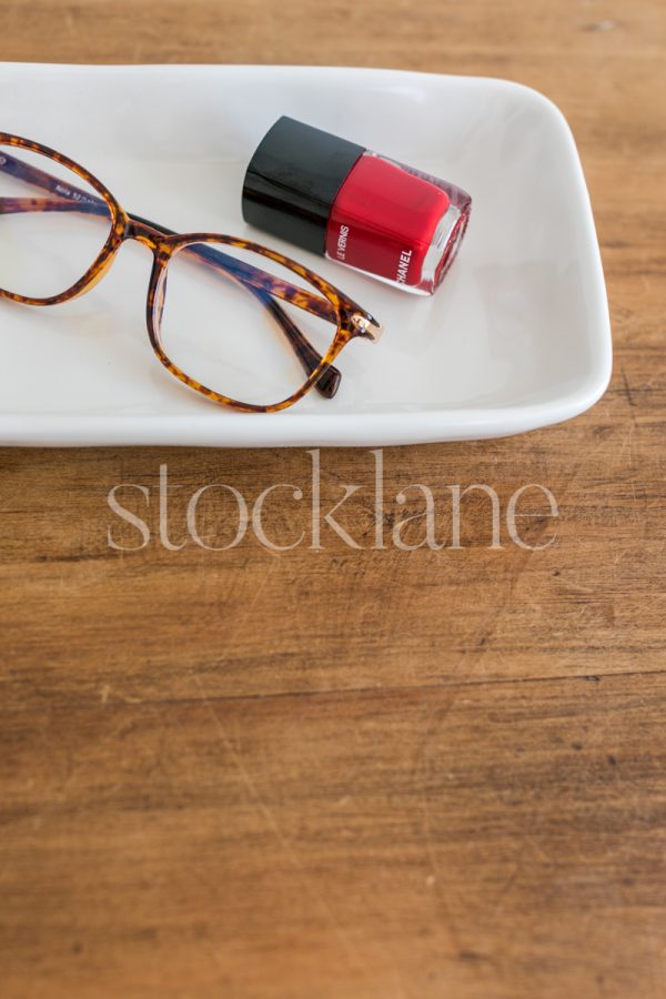 Vertical stock photo of a desk with glasses and red nail polish.