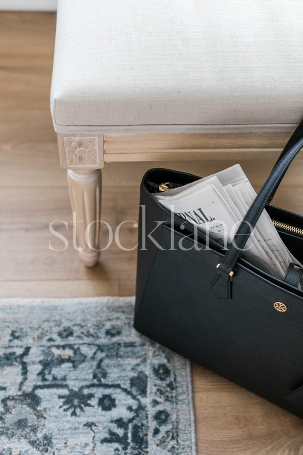 Vertical stock photo of a black handbag with a newspaper.