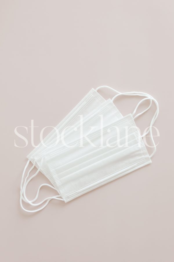 Vertical stock photo of three white masks on a pink background