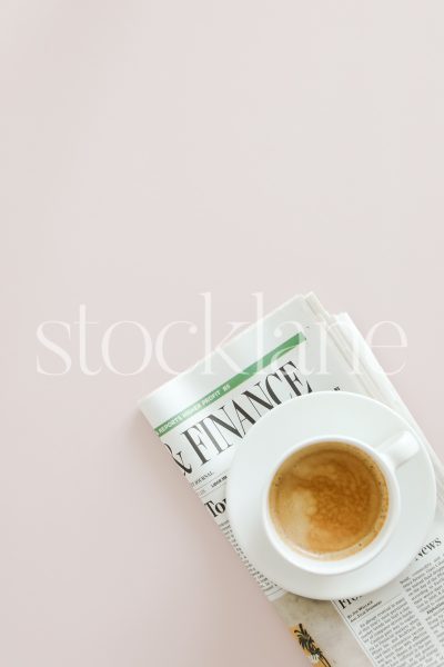 Vertical stock photo of a cup of coffee and a newspaper on a pink background