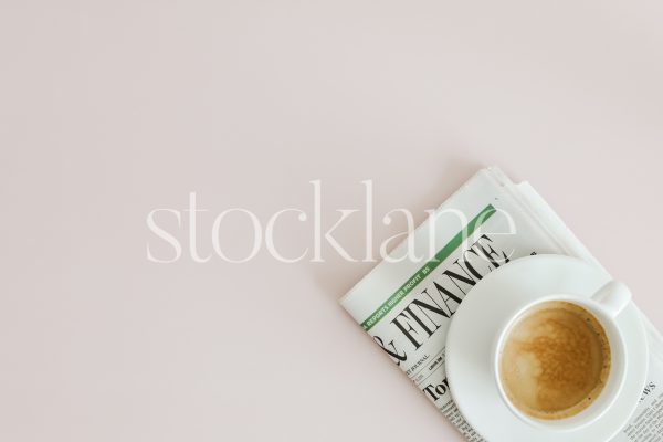 Horizontal stock photo of a cup of coffee and a newspaper on a pink background