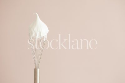 Horizontal stock photo of a whisk with cream on a pink background