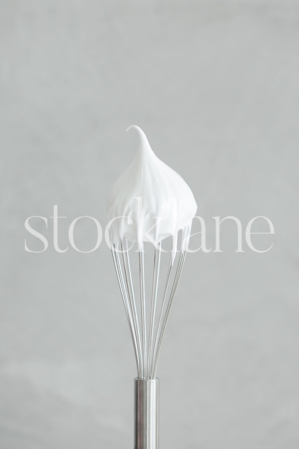 Vertical stock photo of a whisk with cream over a gray background