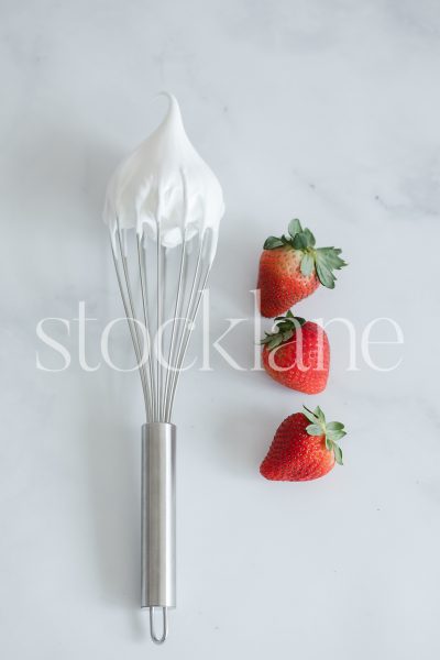 Vertical stock photo of a whisk with cream and strawberries