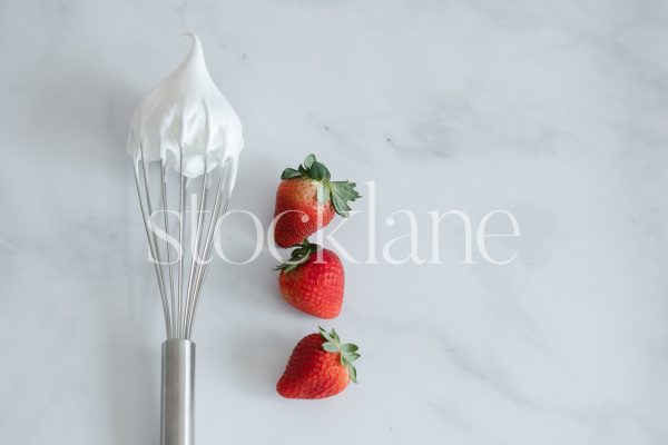 Horizontal stock photo of a whisk with cream and strawberries