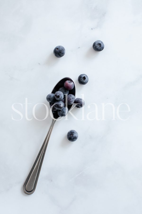 Vertical stock photo of a spoon with blueberries on a marble backfground