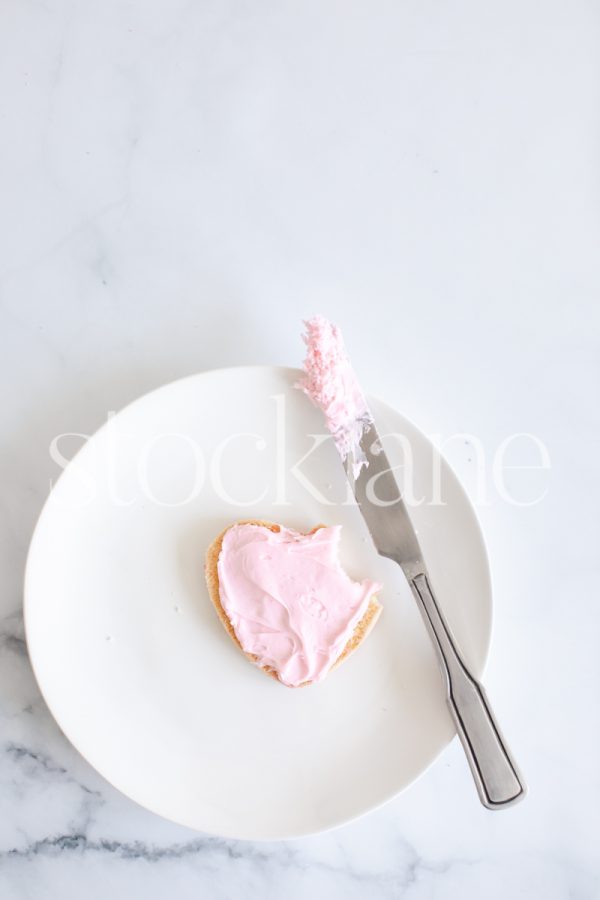 Vertical stock photo of a heart-shaped cookie with pink frosting