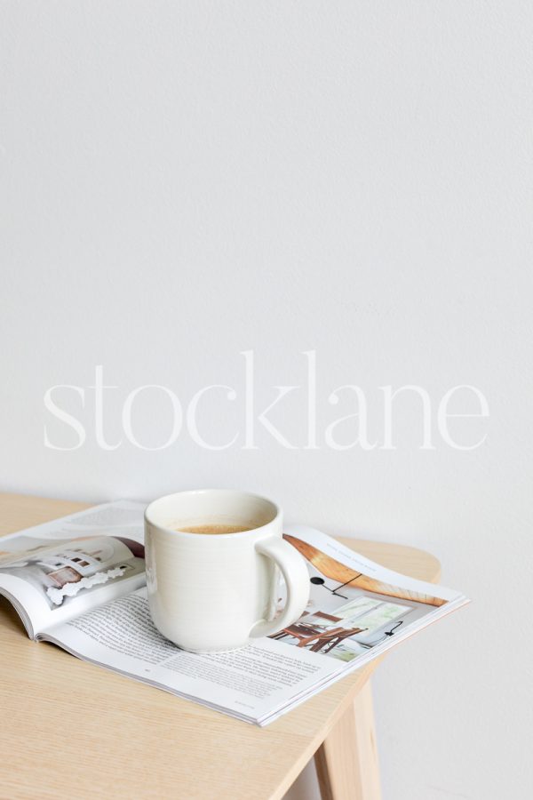 Vertical stock photo of a cup of coffee and a magazine on a table.