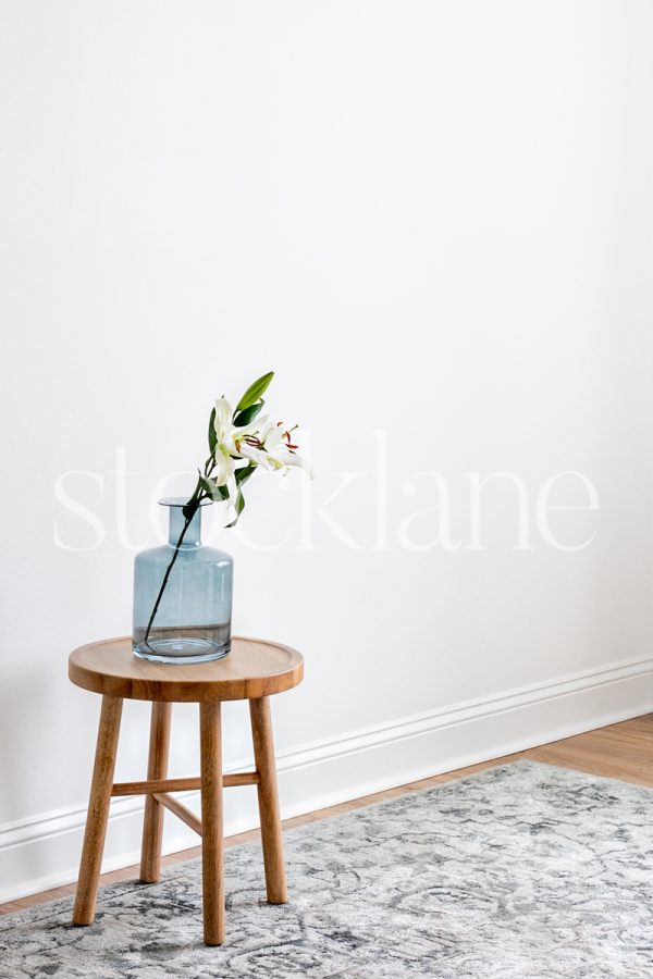 Vertical stock photo of a blue vase with asian lilies on a wood table.