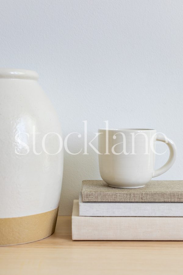 Vertical stock photo of books, a cup of coffee and a decorative vase in neutral colors.