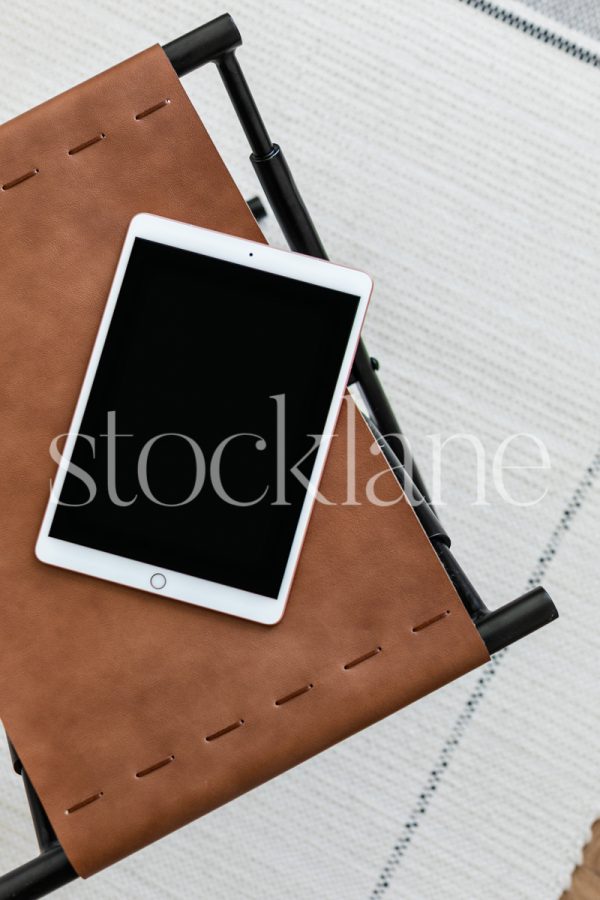 Vertical stock photo of a tablet mockup on a leather ottoman.