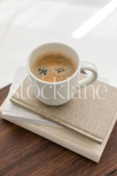 Vertical stock photo of a cup of coffee on a stack of neutral colored books.