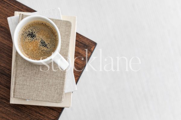 Horizontal stock photo of a coffee cup on a stack of neutral colored books.