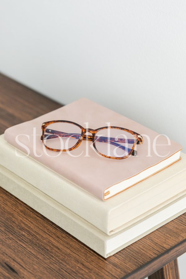 Vertical stock photo of books on a table with a pair of glasses