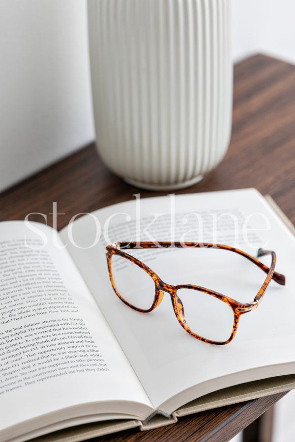 Vertical stock photo of a book on a side table with glasses and a vase