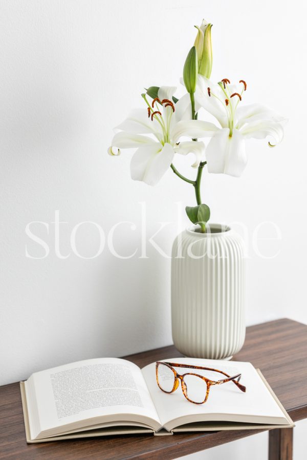 Vertical stock photo of white asian lilies with a book and glasses