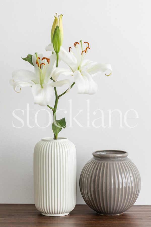 Vertical stock photo of white asian lilies with a white vase and a grey vase