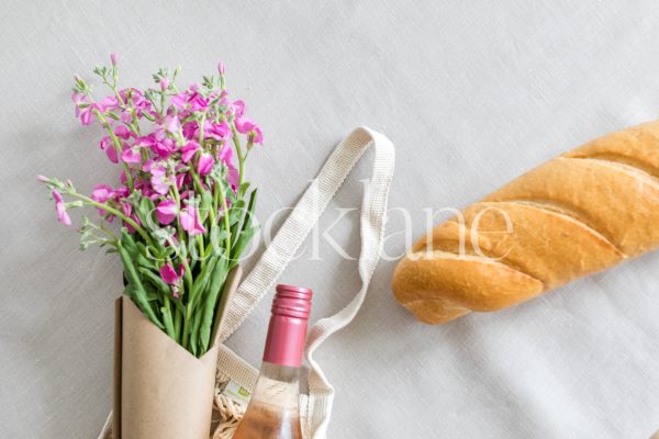 Horizontal stock photo of a pink flower bouquet, a wine bottle and bread.