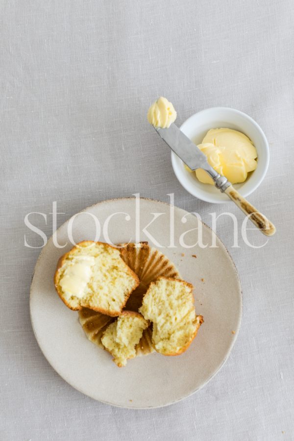 Vertical stock photo of a plate with a muffin and a butter dish.