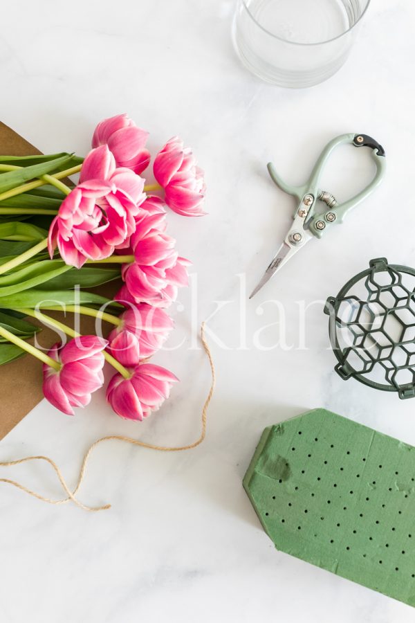 Vertical stock photo of pink tulips and flower arranging tools.