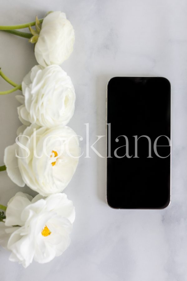 Vertical stock photo of white ranunculus flowers and a phone.