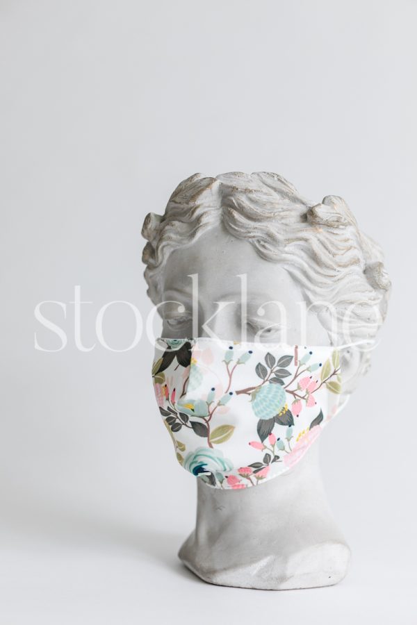 Vertical stock photo of a woman head sculpture with a floral mask.