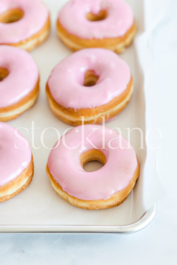 Vertical stock photo of a tray with a pink donuts.