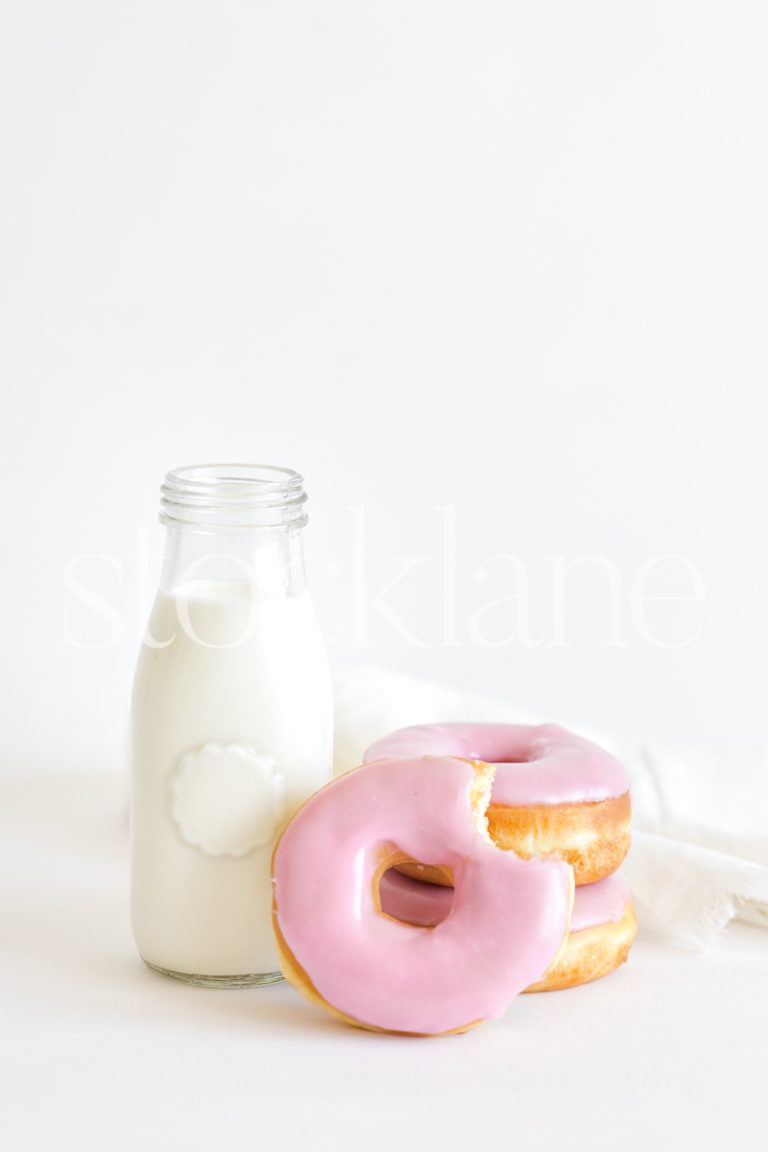 Vertical stock photo of a jar with milk and strawberry frosted donuts.