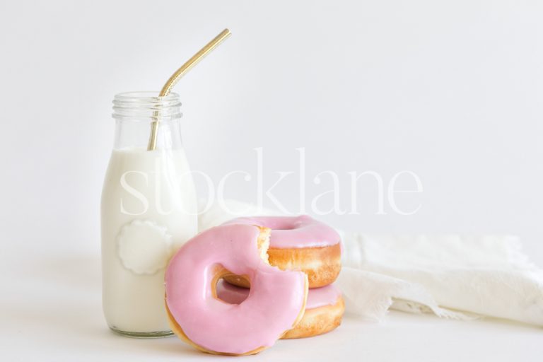 Horizontal stock photo of a jar with milk and strawberry frosted donuts.