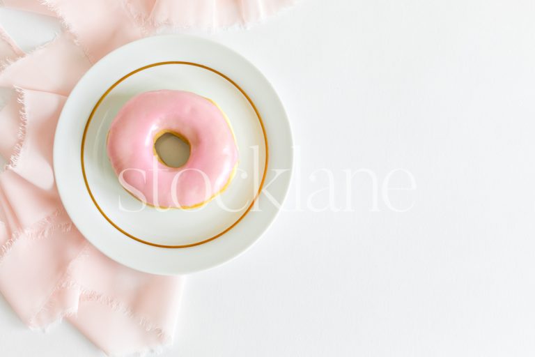 Horizontal stock photo of a pink donut on a plate with a pink and white background.