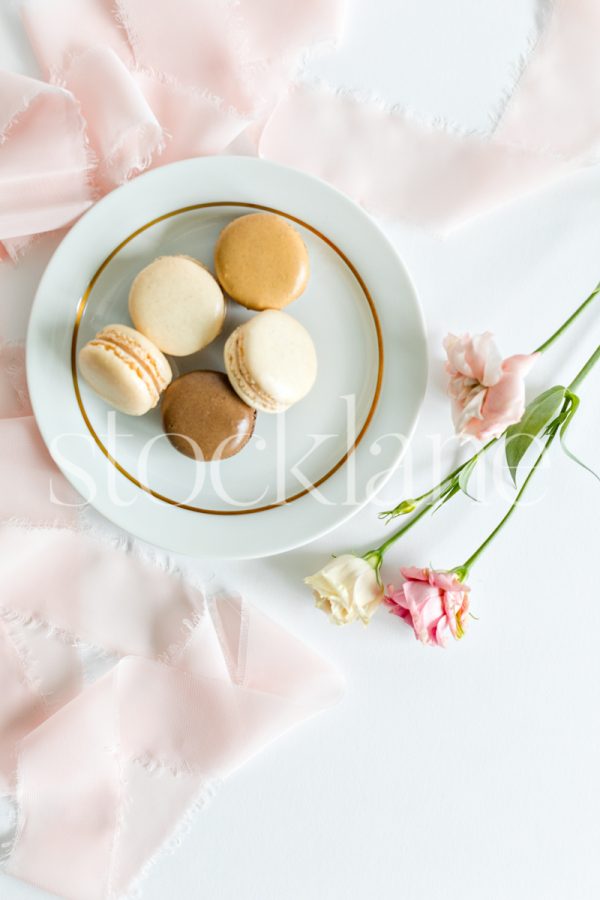 Vertical stock photo of a plate of macarons and pink flowers.