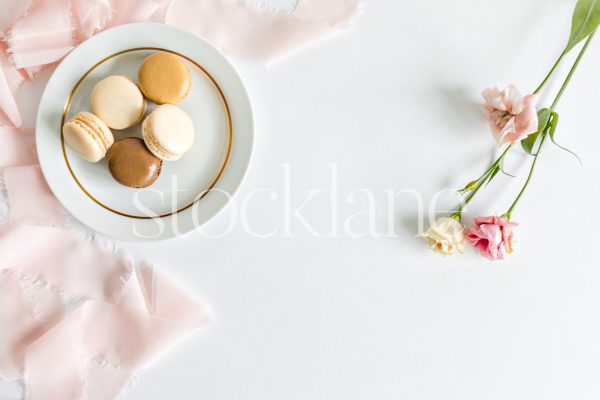 Horizontal stock photo of a plate of macarons and pink flowers.