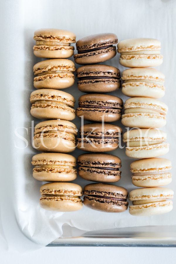 Vertical stock photo of vanilla, chocolate and caramel macarons on a baking tray.