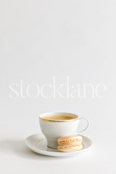 Vertical stock photo of a cup of coffee and a vanilla macaron.