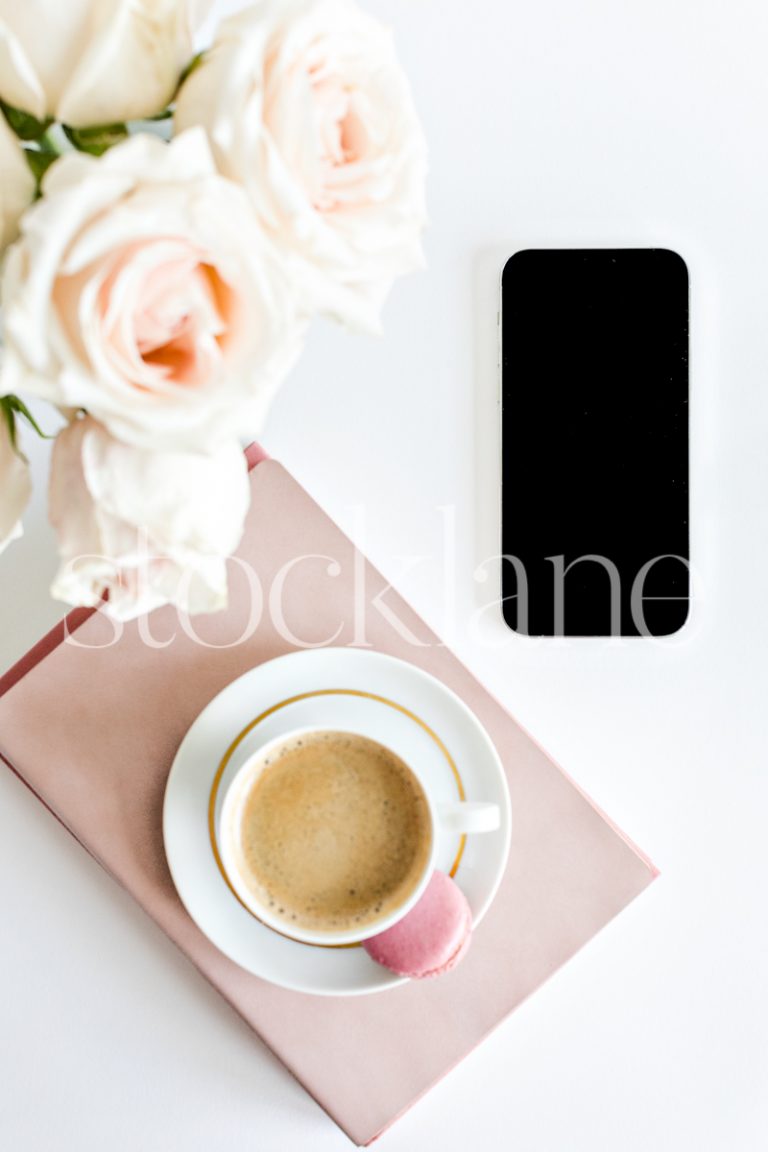 Vertical stock photo of a coffee cup on top of pink books, with a phone and roses.