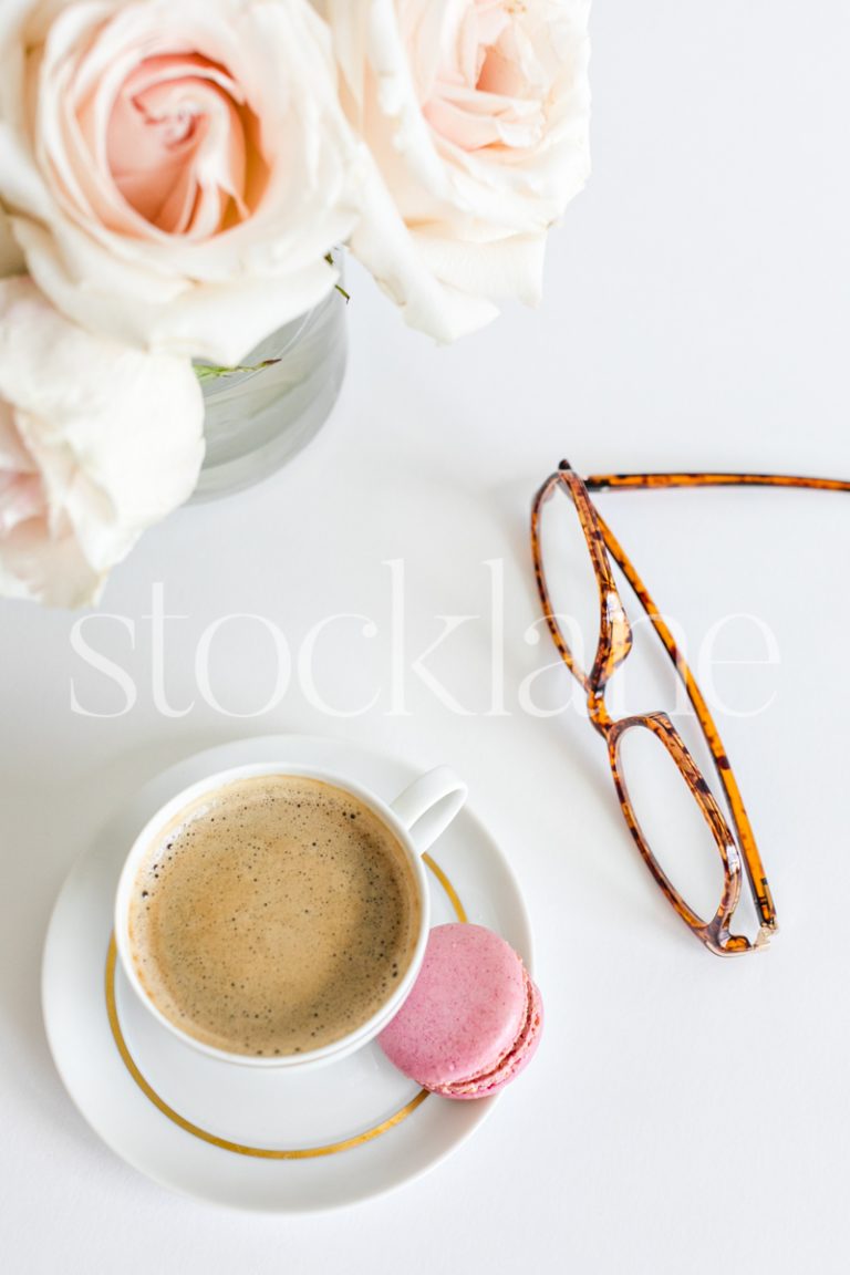 Vertical stock photo of a coffee cup with a pair of glasses and pink roses in the background.