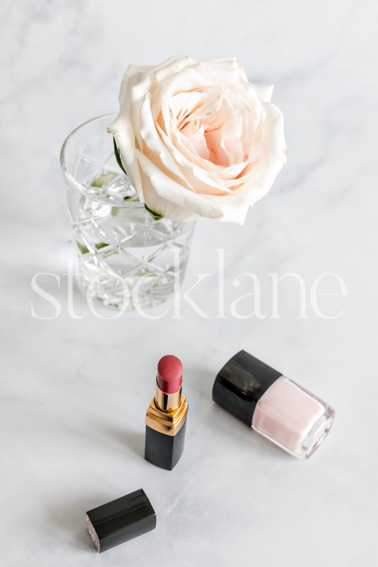 Vertical stock photo of lipstick and nail polish with a pink rose.