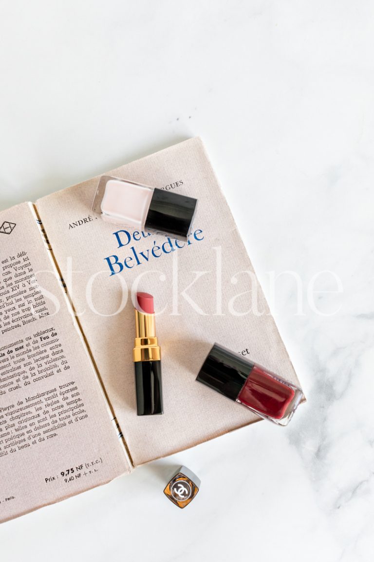 Vertical stock photo of a book with nail polish and lipstick.