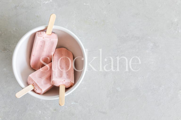 Horizontal stock photo of a bowl with three strawberry popsicles.