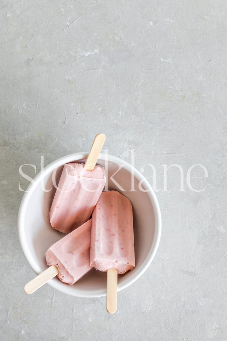 Vertical stock photo of a bowl with three strawberry popsicles.