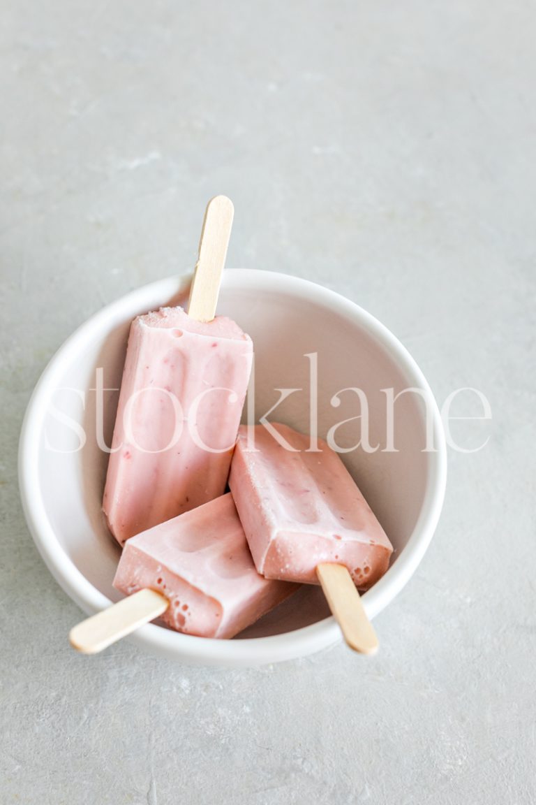 Vertical stock photo of a bowl with three strawberry popsicles.