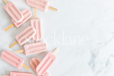 Horizontal stock photo of a bunch of strawberry popsicles on a marble countertop.