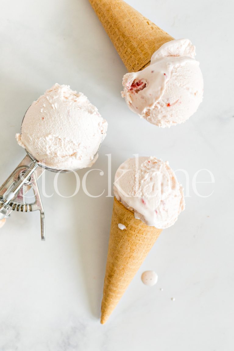 Vertical stock photo of strawberry ice cream cones on a marble countertop.