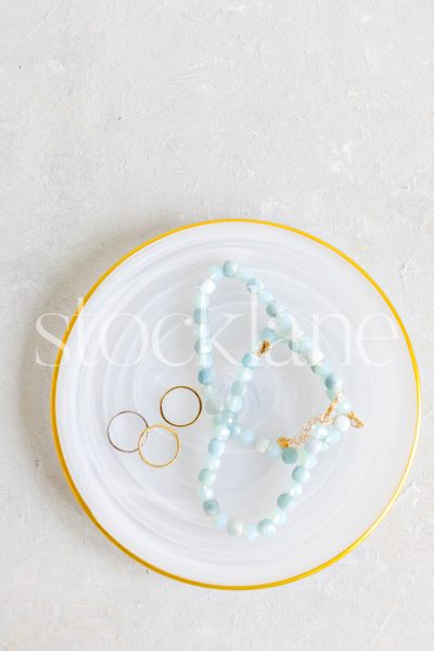 Vertical stock photo of a gold-rimmed plate with jewelry.