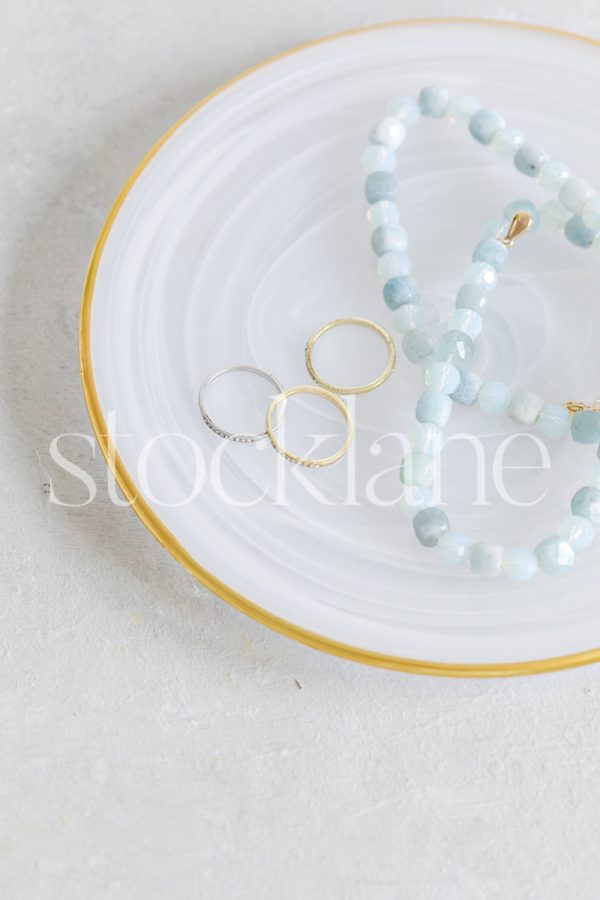 Vertical stock photo of a gold-rimmed plate with jewelry.