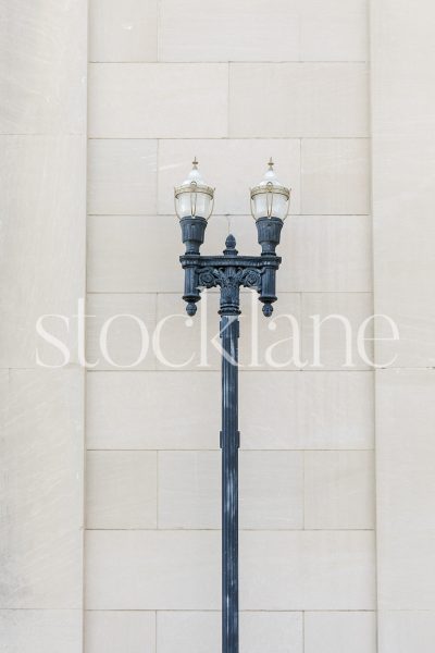 Vertical stock photo of a classic streetlamp in front of a neutral colored wall.