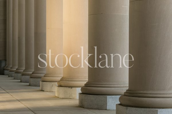 Horizontal stock photo of classic building columns in neutral colors, with sunlight shining through.