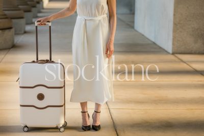 Horizontal stock photo of a woman in a white dress holding a suitcase.