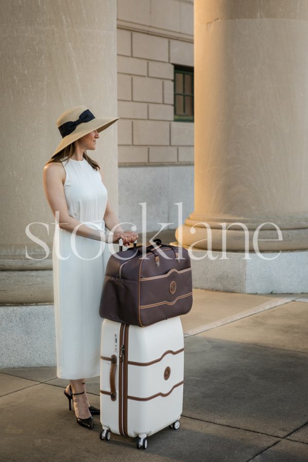 Vertical stock photo of a woman in a white dress with a suitcase.