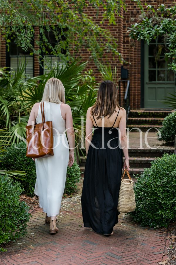 Vertical stock photo of two women walking towards the entrance of a home.